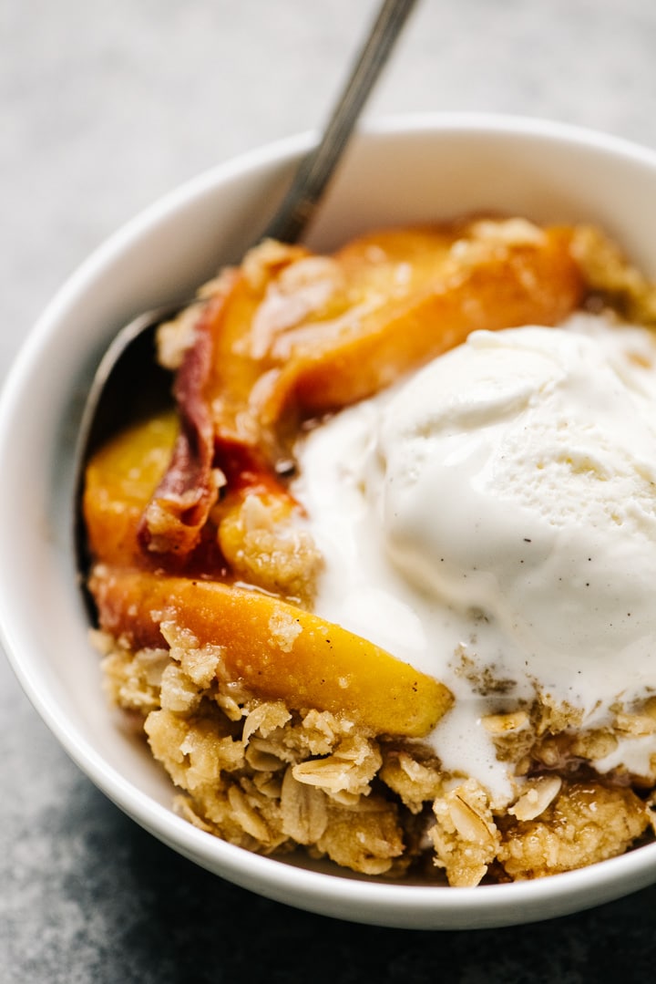 Side view, a bowl of warm peach crisp topped with vanilla ice cream. 