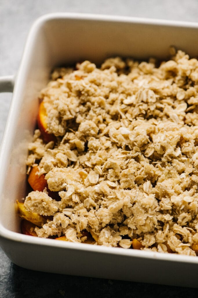 Fresh peaches in a casserole dish topped with gluten free crisp topping.