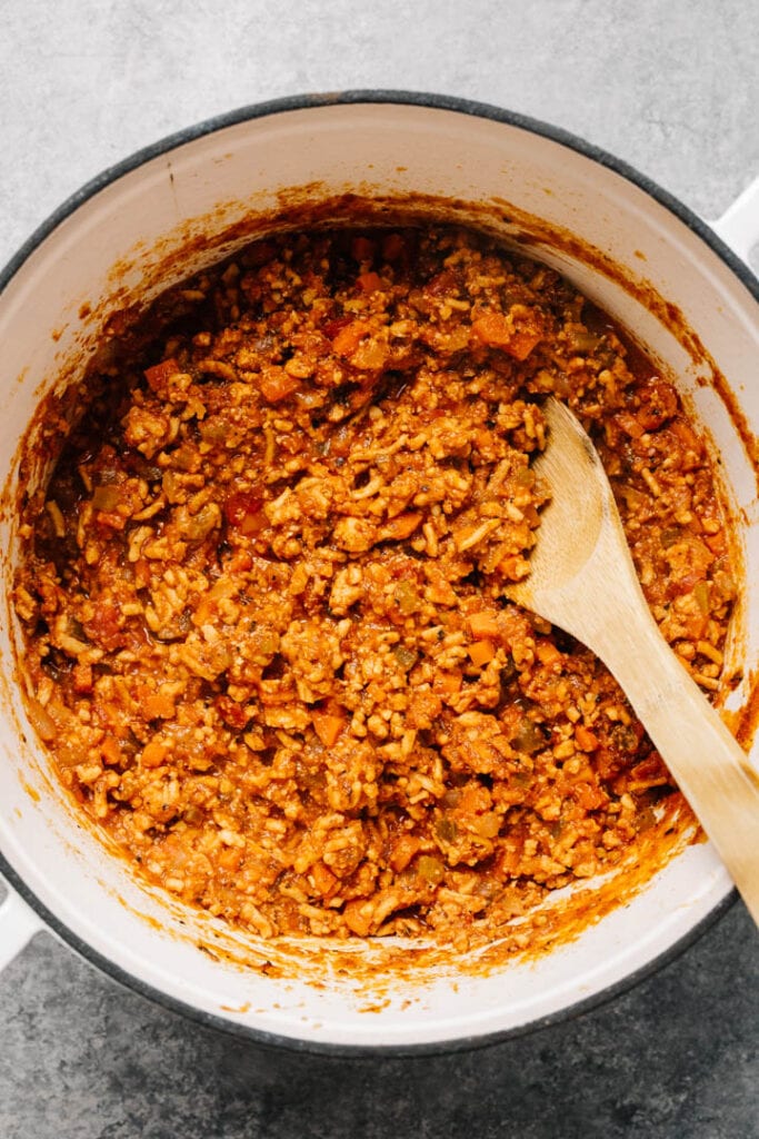 A pot of bolognese sauce cooking with a wooden spoon. 