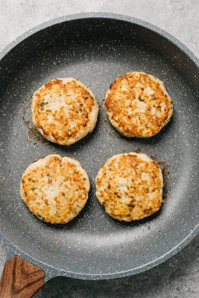 Pan-seared ground chicken burgers in a non-stick skillet.