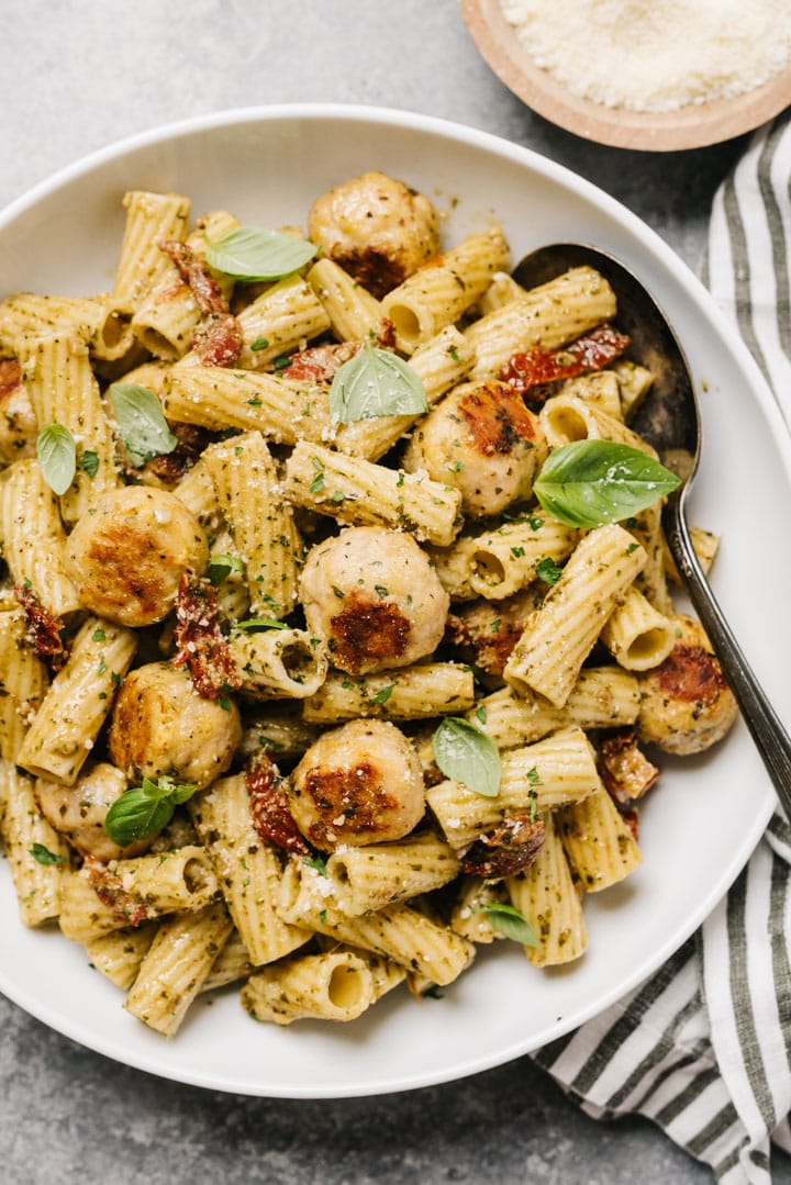 A large bowl of pesto pasta with chicken meatballs. 