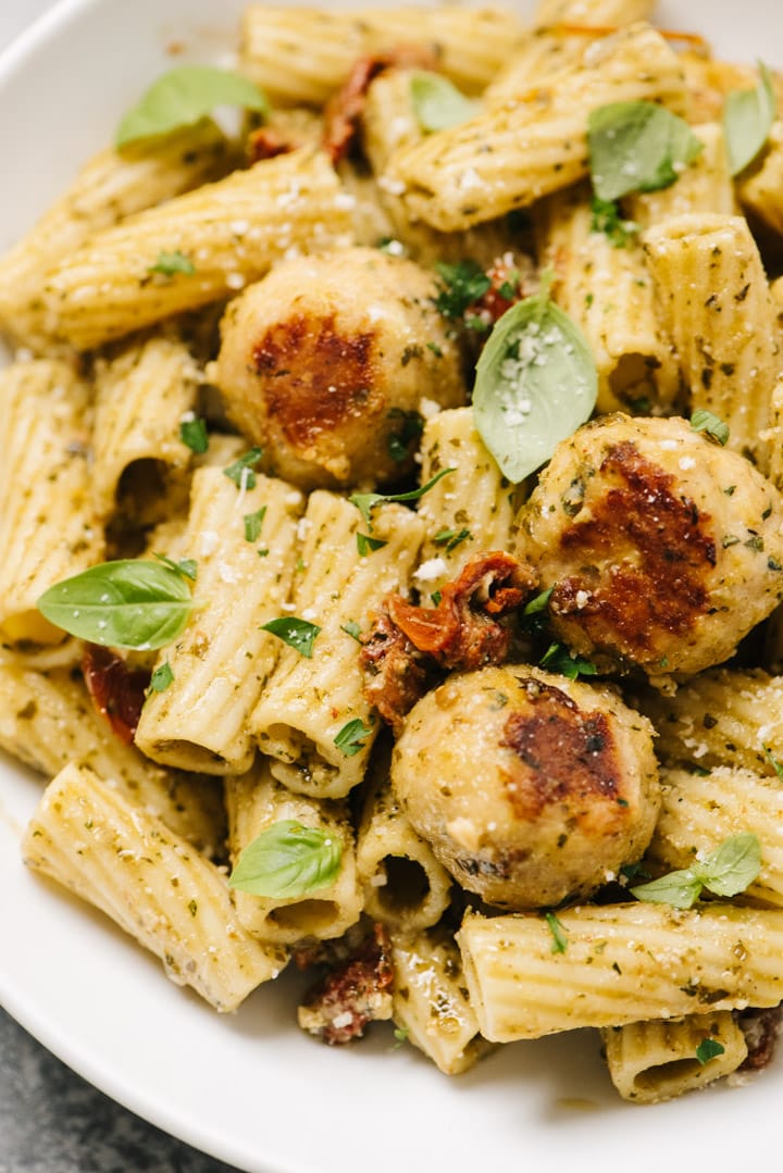 Side view, pesto pasta with chicken meatballs in a white pasta bowl.