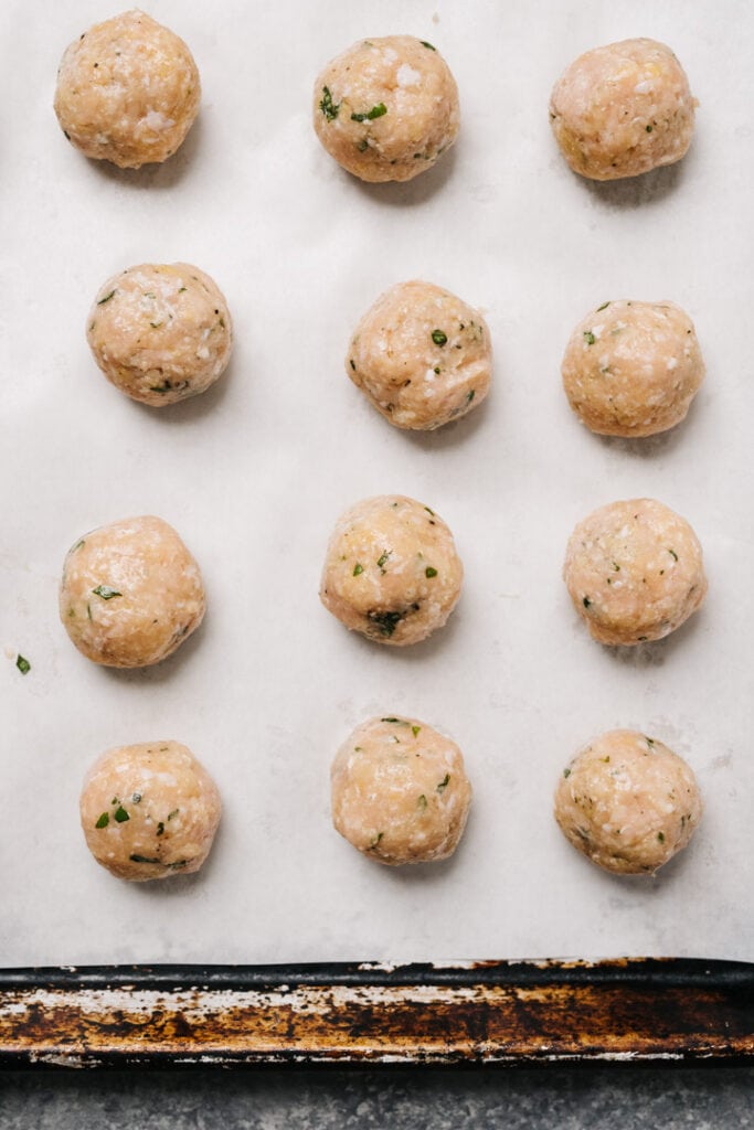Chicken meatballs arranged on a parchment lined baking sheet.