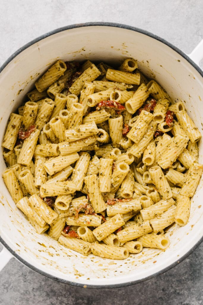 Pasta, pesto sauce, sun-dried tomatoes, and garlic tossed in a white post.