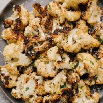 Parmesan roasted cauliflower on a dark grey plate, garnished with chopped parsley and finely grated parmesan cheese.