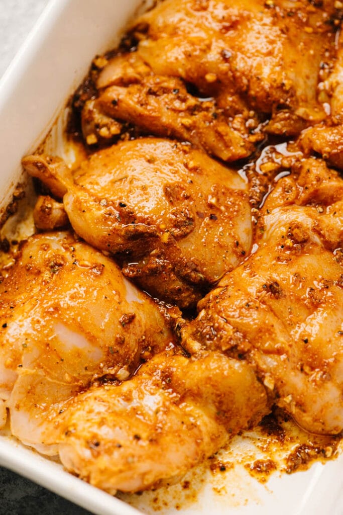 Boneless chicken thighs covered in taco marinade in a casserole dish.