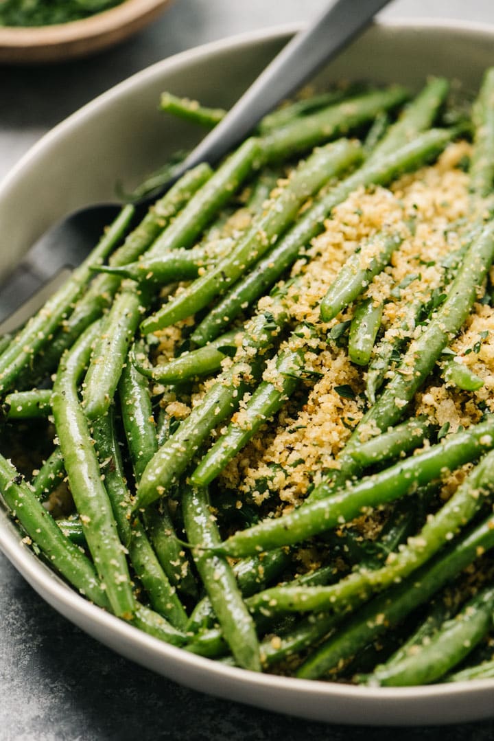 Side view, Italian green beans in a low tan serving bowl with a black serving fork.