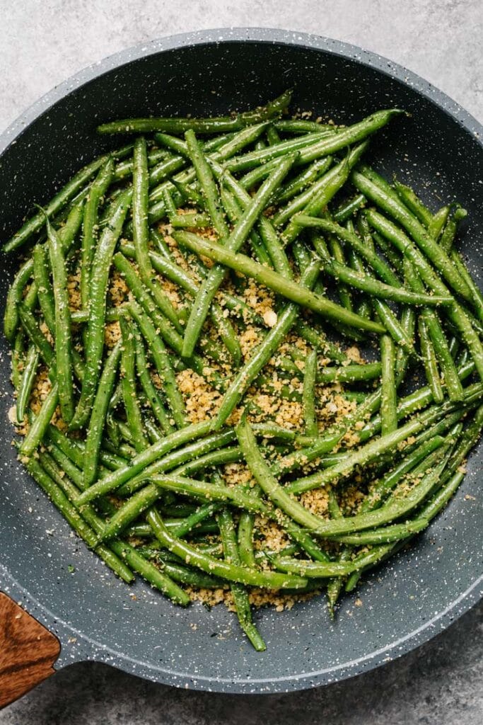 Steamed green beans tossed with parmesan bread crumbs in a skillet.