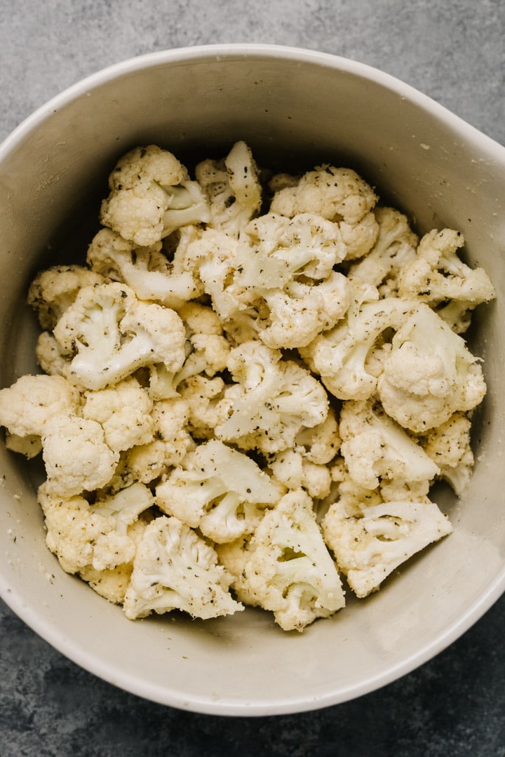 Cauliflower florets in a bowl tossed with olive oil, parmesan cheese, Italian seasoning, garlic powder, salt, and pepper.