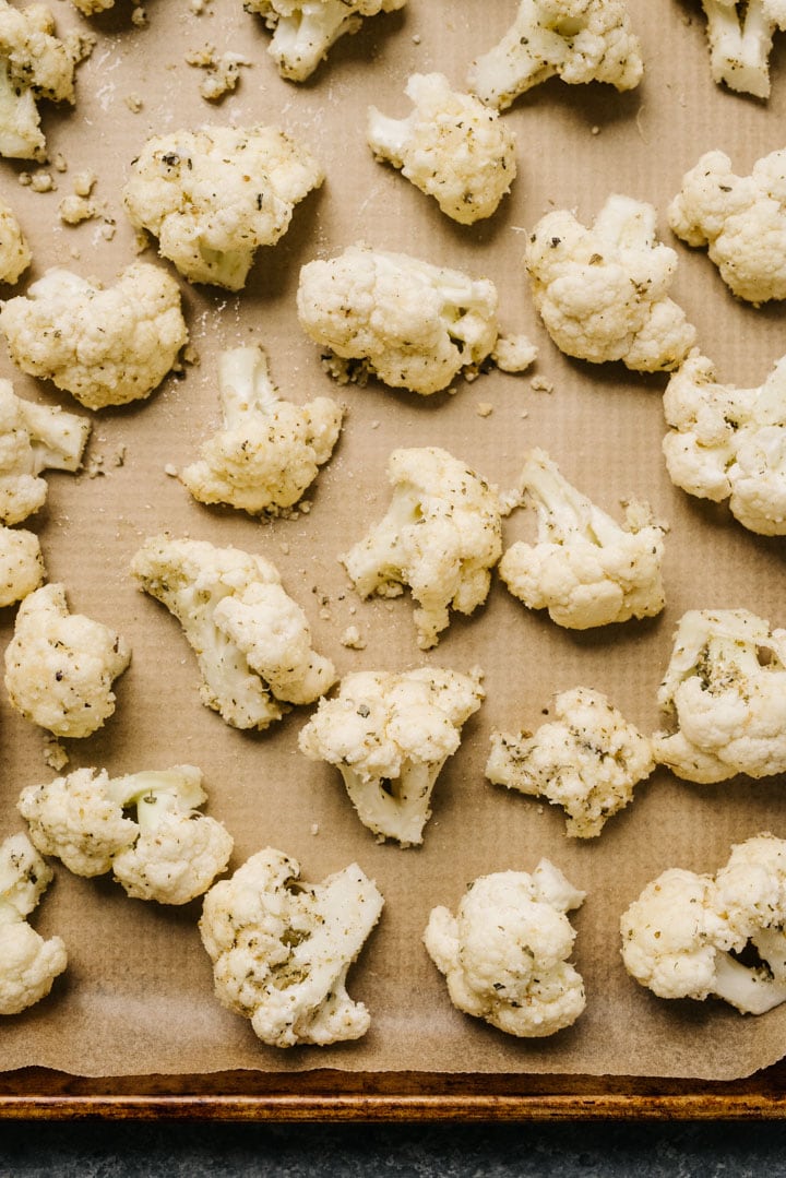 Cauliflower seasoned with parmesan cheese and herbs on a parchment lined baking sheet.