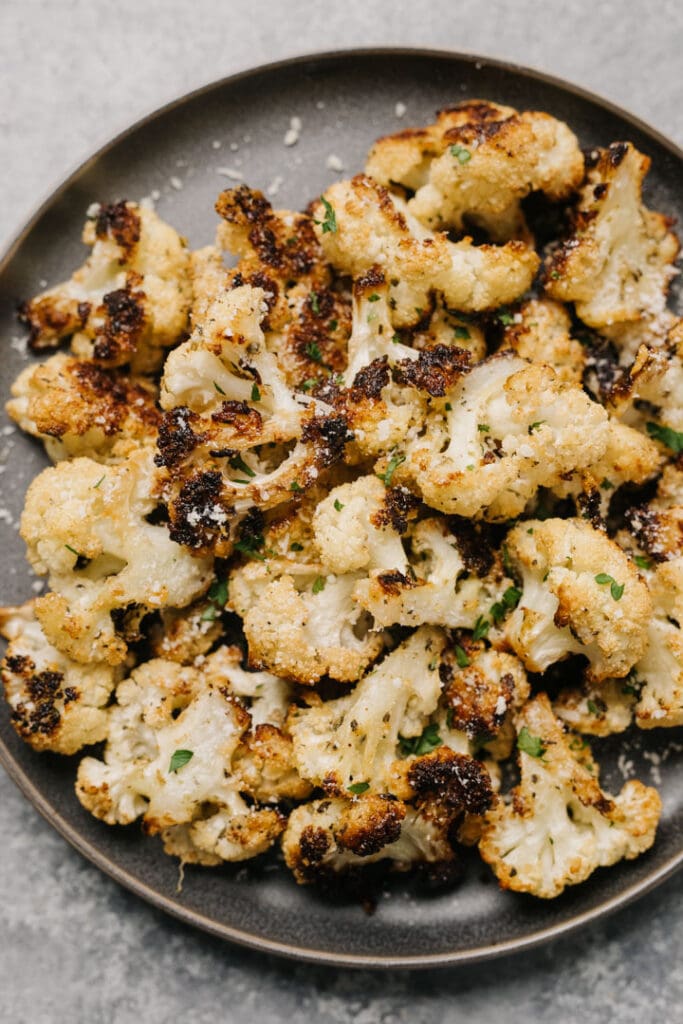 Parmesan roasted cauliflower on a dark grey plate, garnished with chopped parsley and finely grated parmesan cheese.