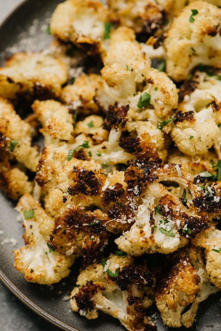 Side view, parmesan roasted cauliflower on a grey serving platter, garnished with fresh herbs.