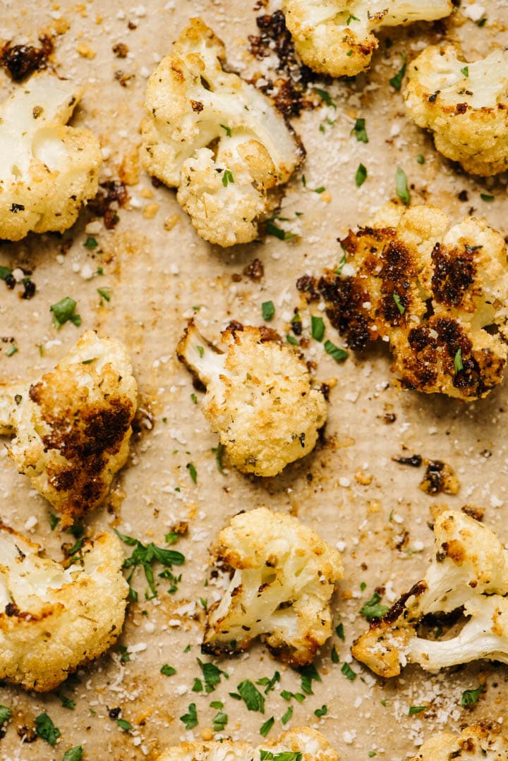 Parmesan roasted cauliflower florets on a sheet pan, garnished with fresh herbs and more grated parmesan cheese.