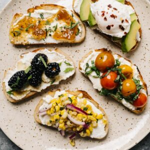 Ricotta toast with different toppings on a brown speckled plate.