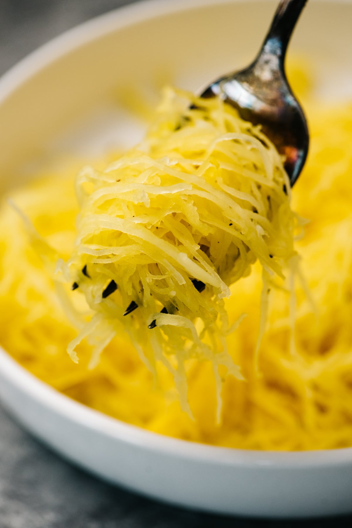 Side view, spaghetti squash noodles wrapped around a serving fork hovering over a bowl.