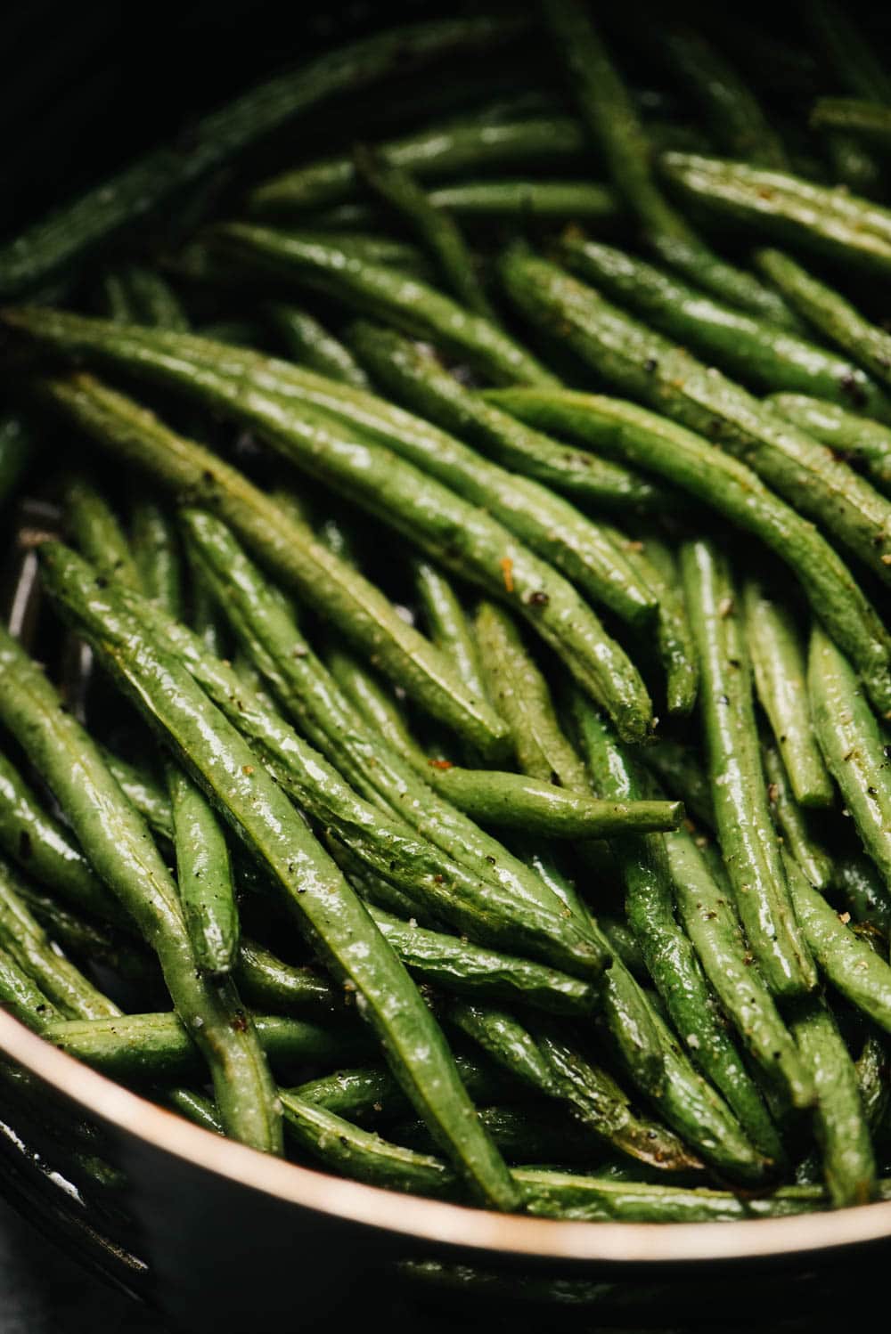 Side view, cooked green beans in the basket of an air fryer.