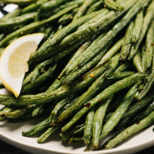 Air fryer green beans on a plate with a lemon wedge.