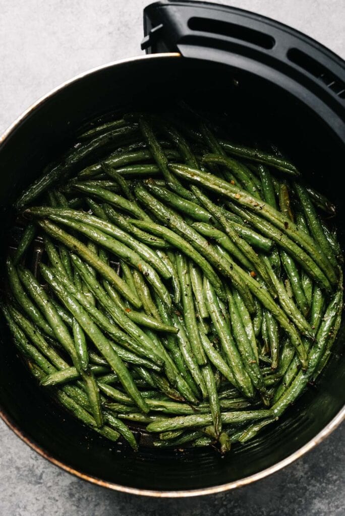 Cooked green beans in the basket of an air fryer.