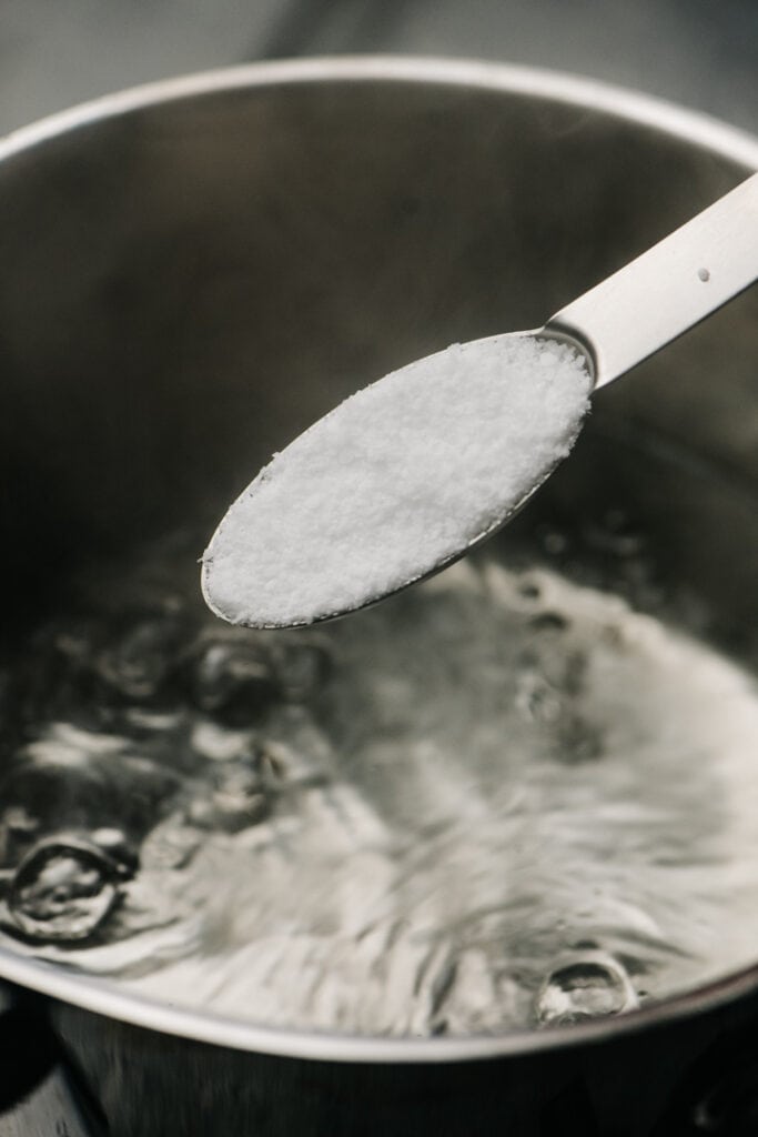 A spoon of salt being poured into boiling water.