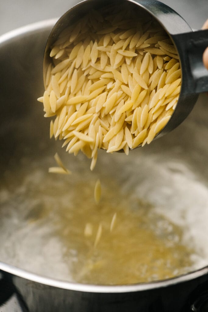 Orzo being poured into boiling water.
