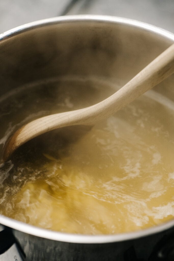 Orzo cooking in a pot with a wooden spoon stirring.