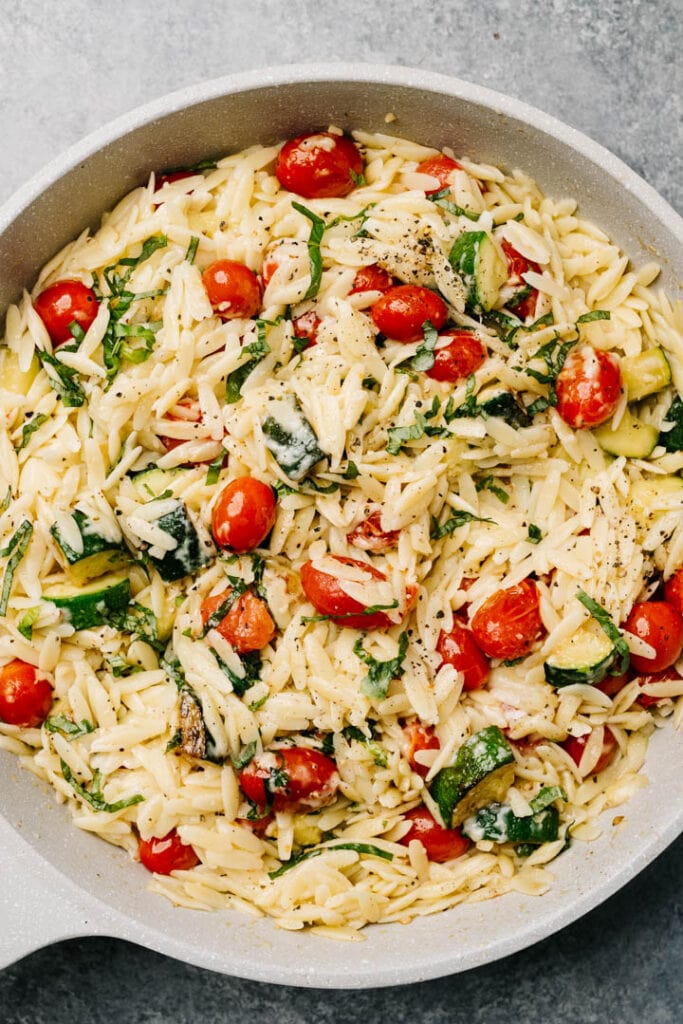 Creamy parmesan risotto with tomatoes, zucchini, and basil in a grey skillet.