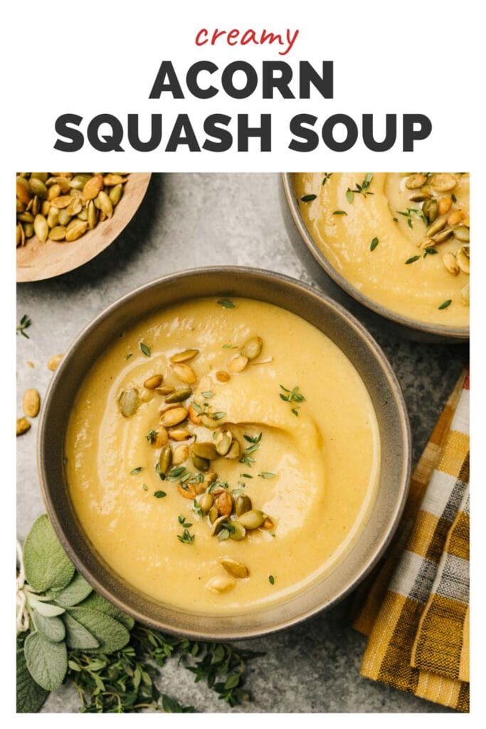 A bowl of acorn squash soup garnished with roasted pepitas and fresh sage surrounded by a plaid napkin, fresh sage and more soup and a bowl of pepitas, with a top banner that reads creamy acorn squash soup.