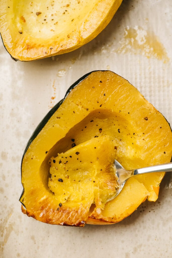A roasted acorn squash half with a spoon scooping out the flesh. 