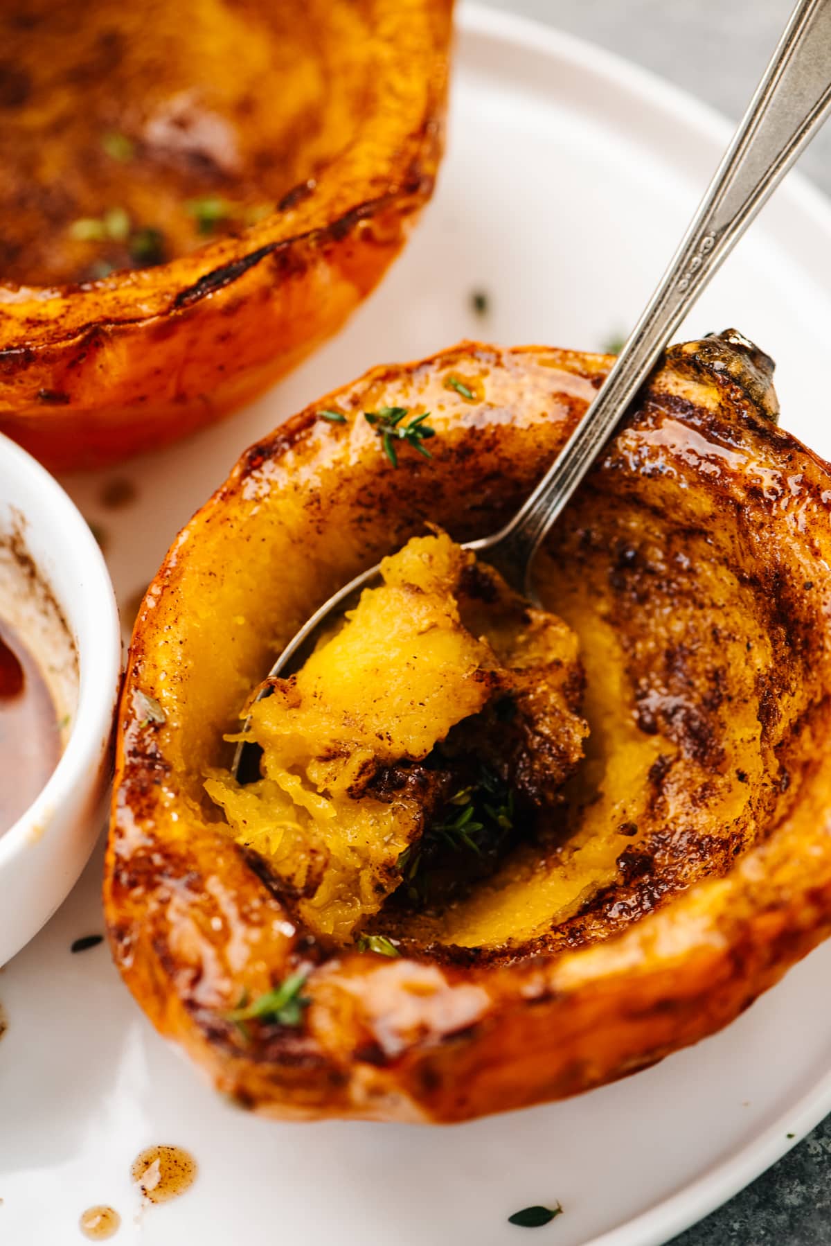 Side view, air fryer acorn squash halves on a white plate with a spoon tucked into the flesh.
