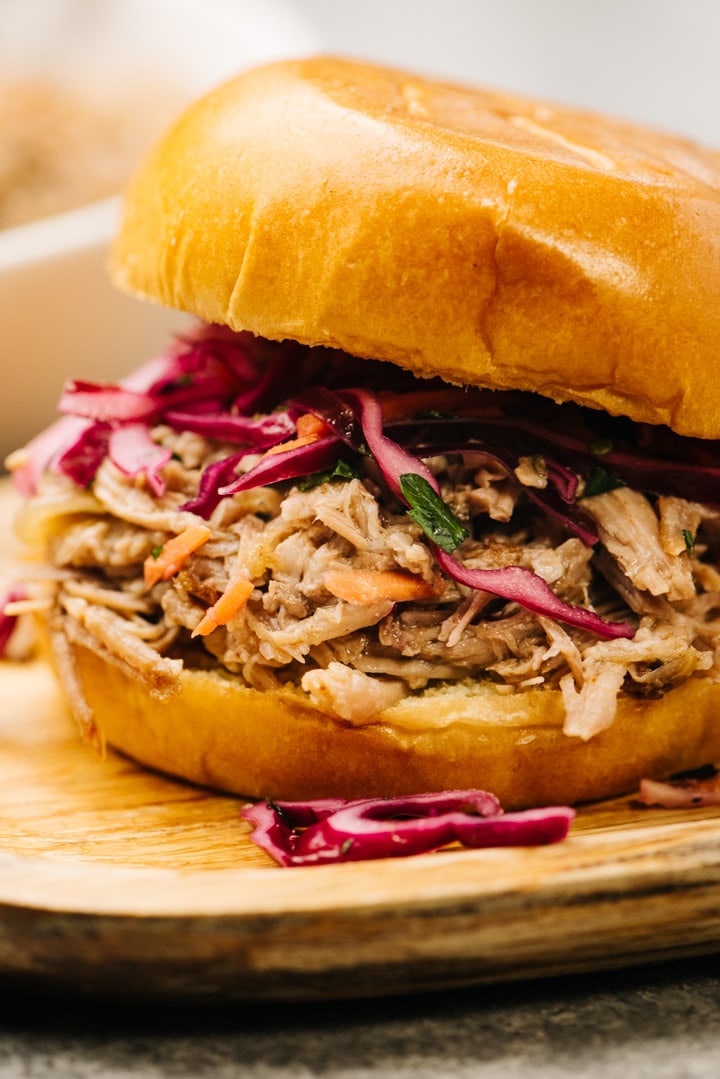 Side view, pulled pork sandwich topped with vinegar coleslaw on a wood platter.