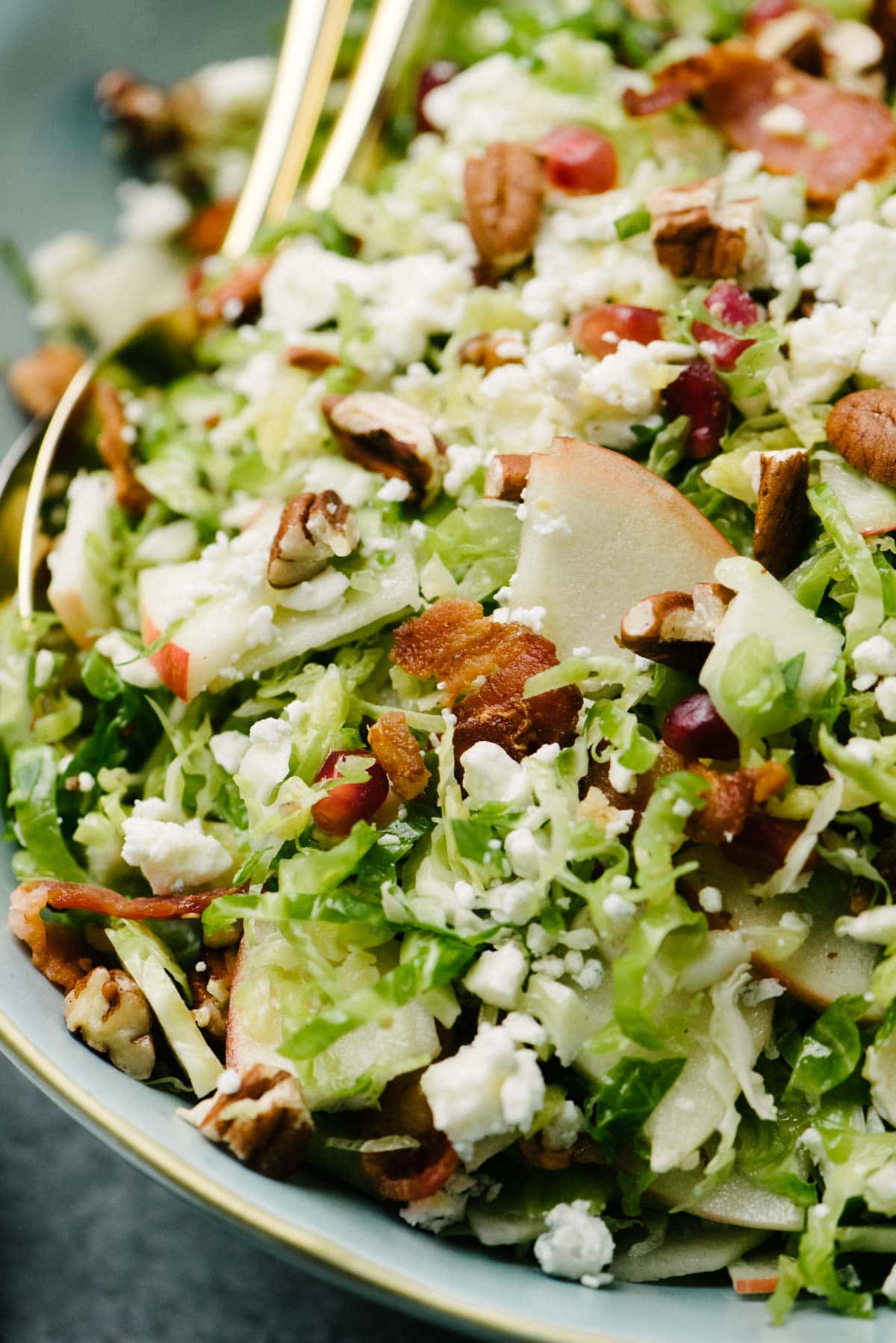 Side view, Brussels sprout salad with bacon, apples, pomegranates, pecans, and blue cheese in a large blue salad bowl.