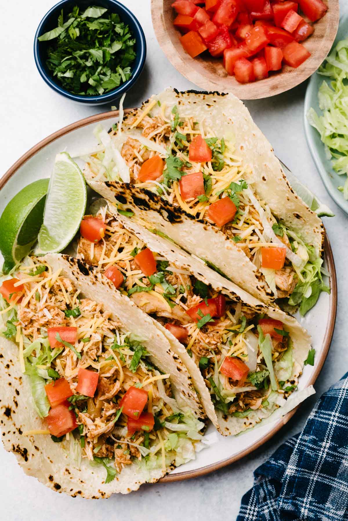 Three crockpot chicken tacos on a plate with small bowls of garnishes to the side.