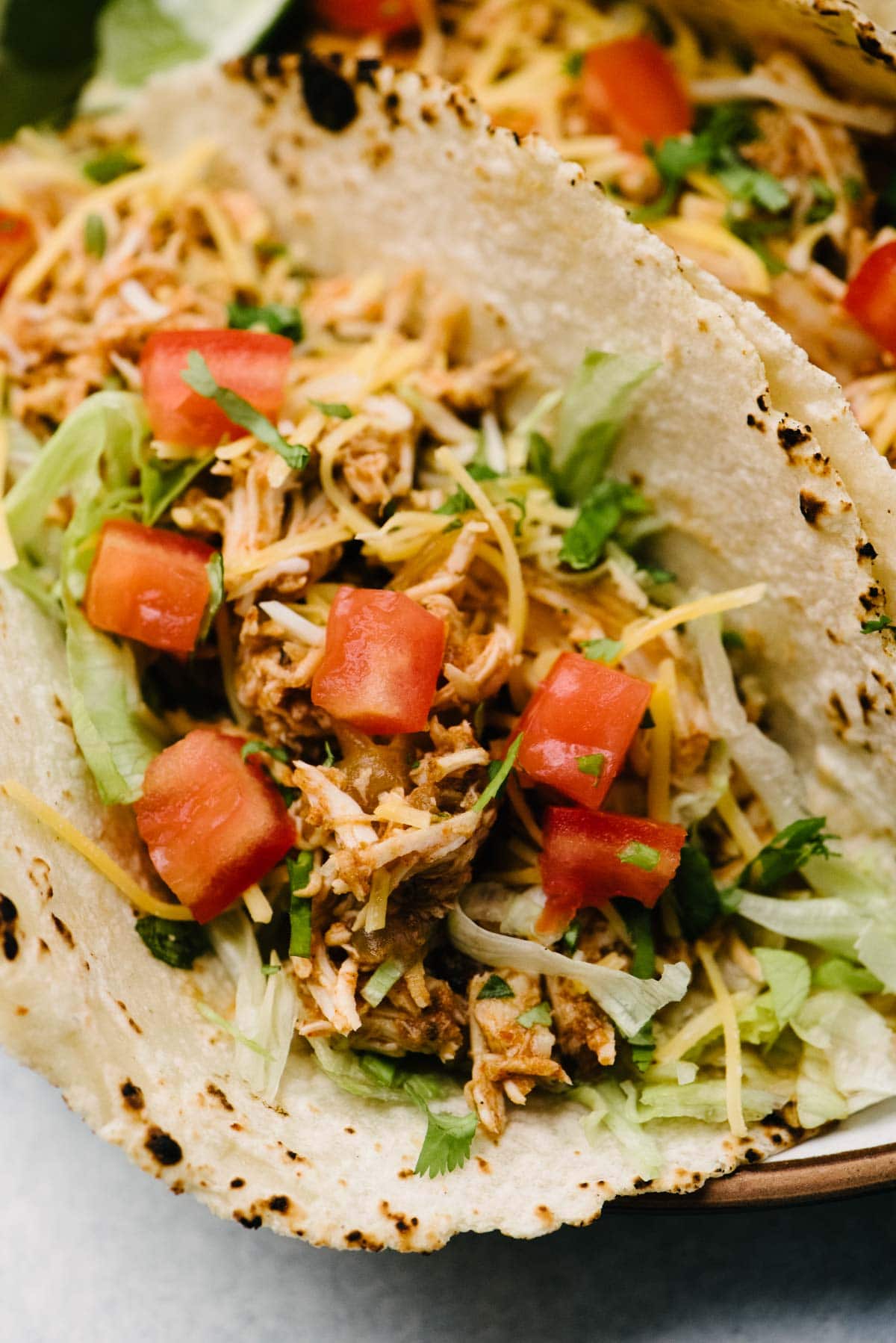 Side view, a crockpot chicken taco on a plate, topped with lettuce, tomato, cheese, and cilantro.