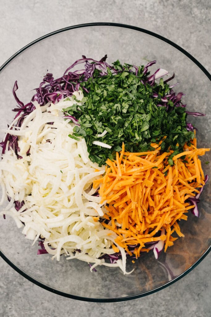 Shredded cabbage, shredded carrots, thinly sliced fennel, and chopped fresh parsley in a large white mixing bowl.