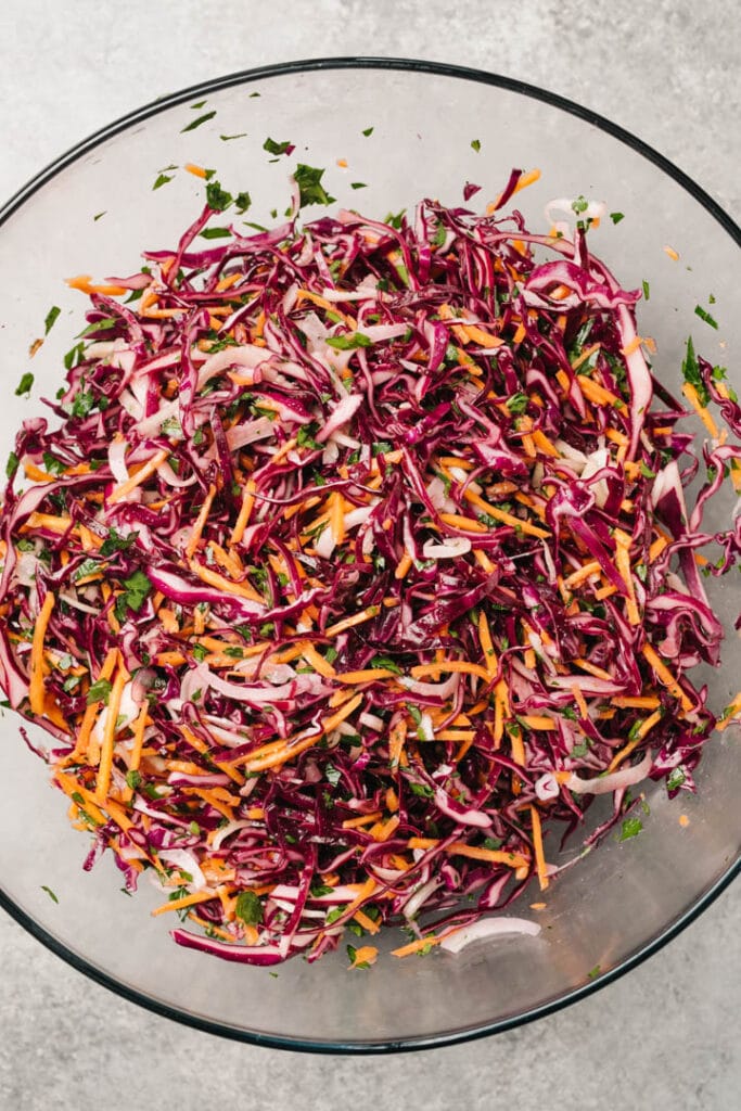 Apple cider vinegar coleslaw tossed with vinaigrette in a large glass mixing bowl.