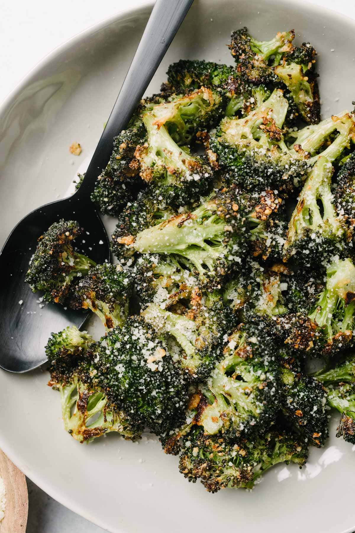 A black serving spoon tucked into a bowl of garlic parmesan roasted broccoli.
