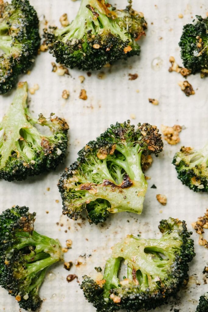 Garlic parmesan roasted broccoli florets on a parchment lined baking sheet.