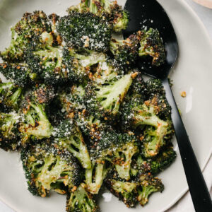 A white plate with parmesan roasted broccoli and a serving spoon.