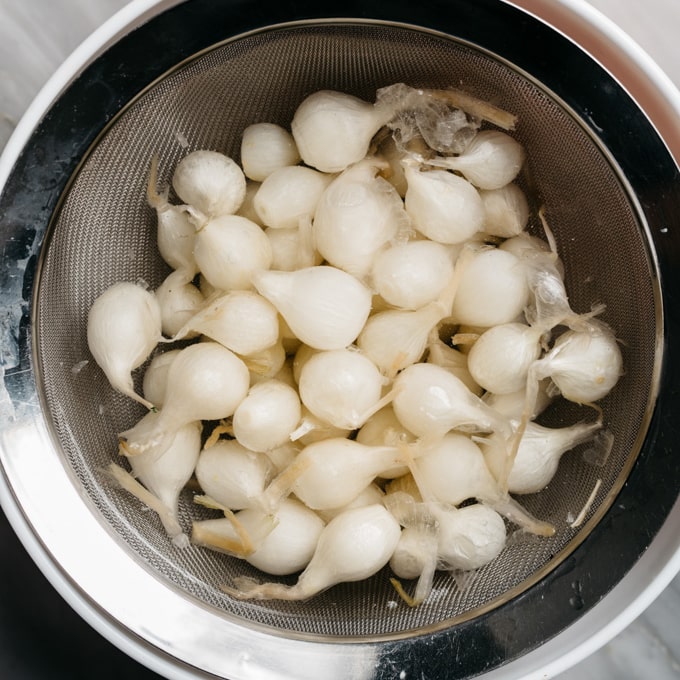 Blanched pearl onions in a mesh strainer.