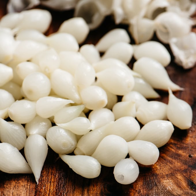 From the side, blanched and peeled pearl onions on a cutting board.