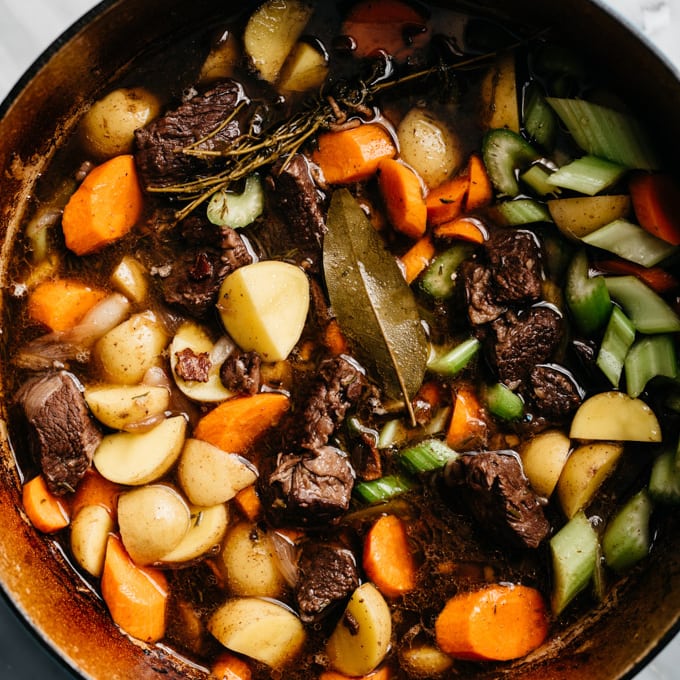 Potatoes, carrots, and celery added to red wine beef stew in a dutch oven.