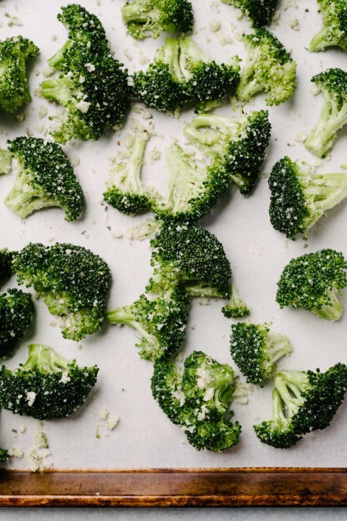 Raw garlic parmesan broccoli florets on a parchment lined baking sheet.