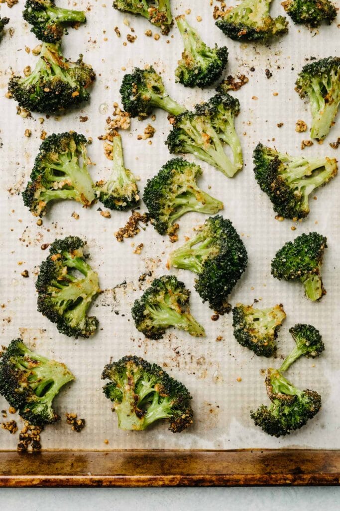 Garlic parmesan roasted broccoli florets on a parchment lined baking sheet.