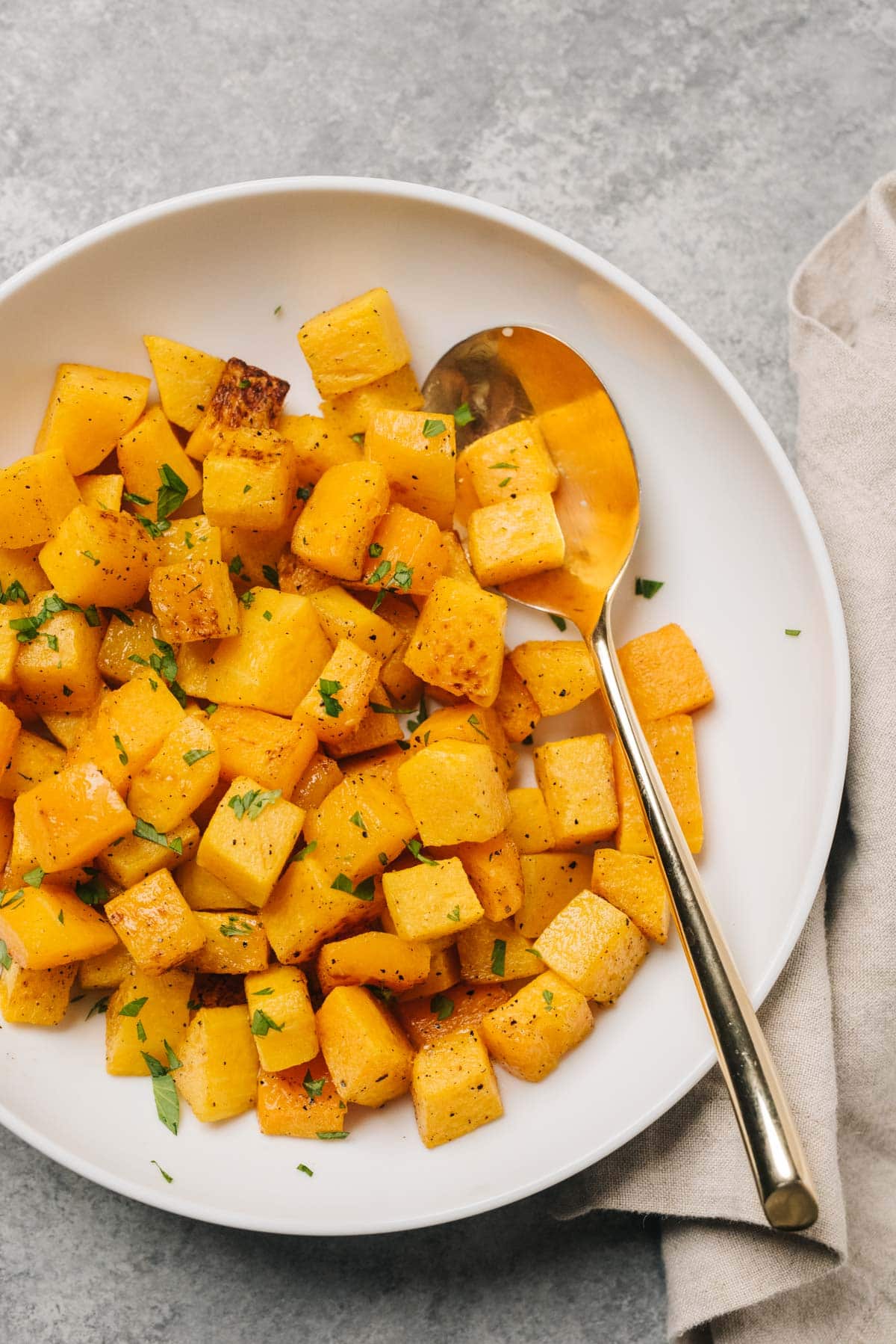 Cubed and roasted butternut squash in a white bowl with seasoning and a spoon.