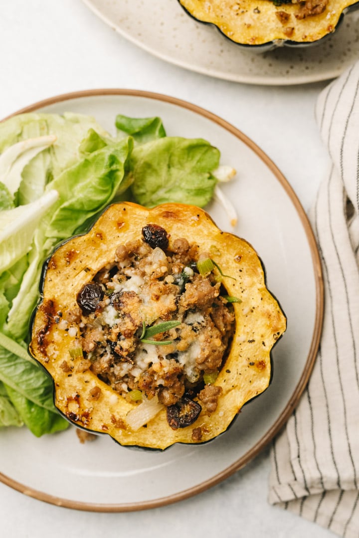Sausage stuffed acorn squash on a plate with a green salad and striped linen napkin to the side.