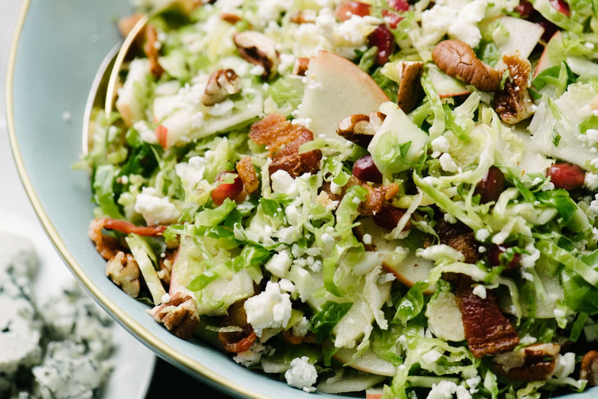 Side view, Brussels sprout salad with bacon, apples, and blue cheese in a large blue salad bowl.