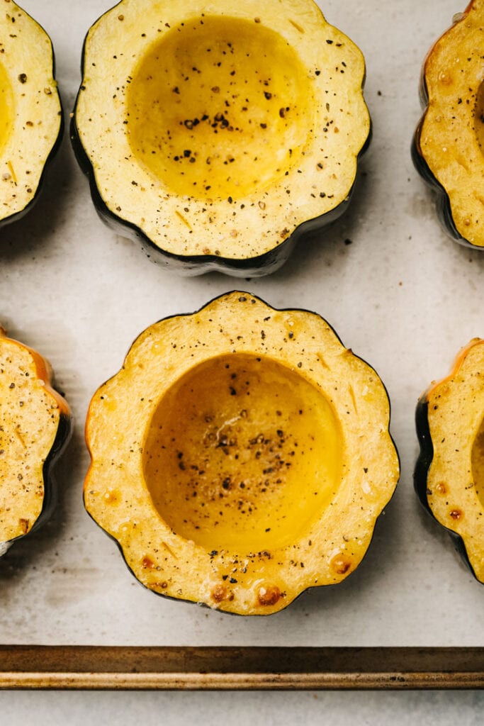 Roasted acorn squash halves seasoned with salt and pepper on a parchment lined baking sheet.