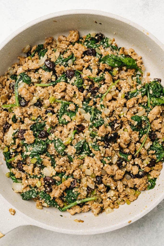 Sausage stuffing for acorn squash in a skillet made with Italian sausage, onions, celery, cranberries, spinach, sage, rosemary, and parmesan cheese.
