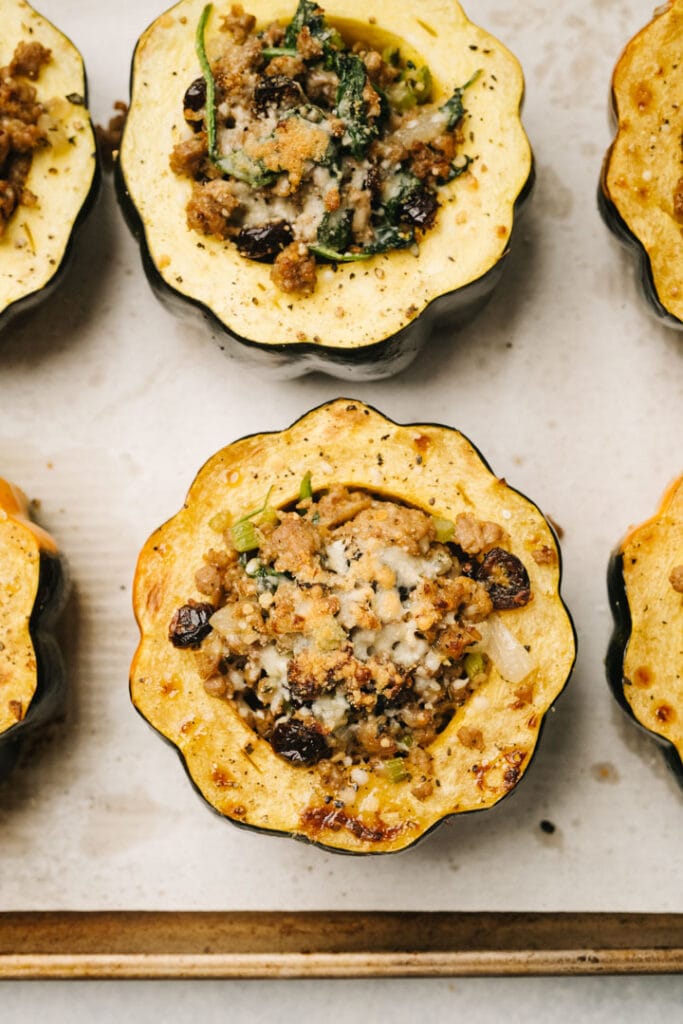 Stuffed acorn squash with sausage stuffing and parmesan cheese on a parchment lined baking sheet.
