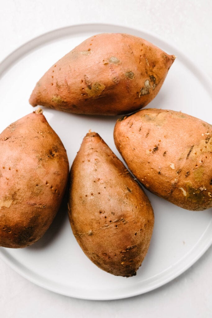 4 whole sweet potatoes on a white plate. 